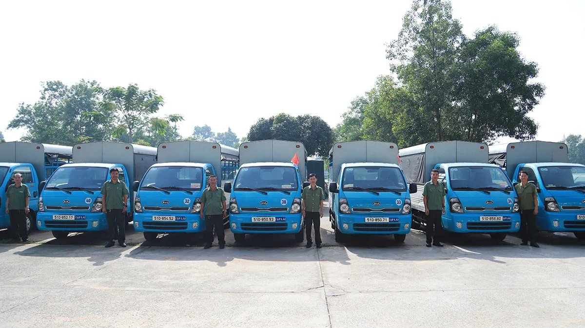 Dàn xe tải tập lái màu xanh xếp thành hàng, giáo viên đứng cạnh từng xe