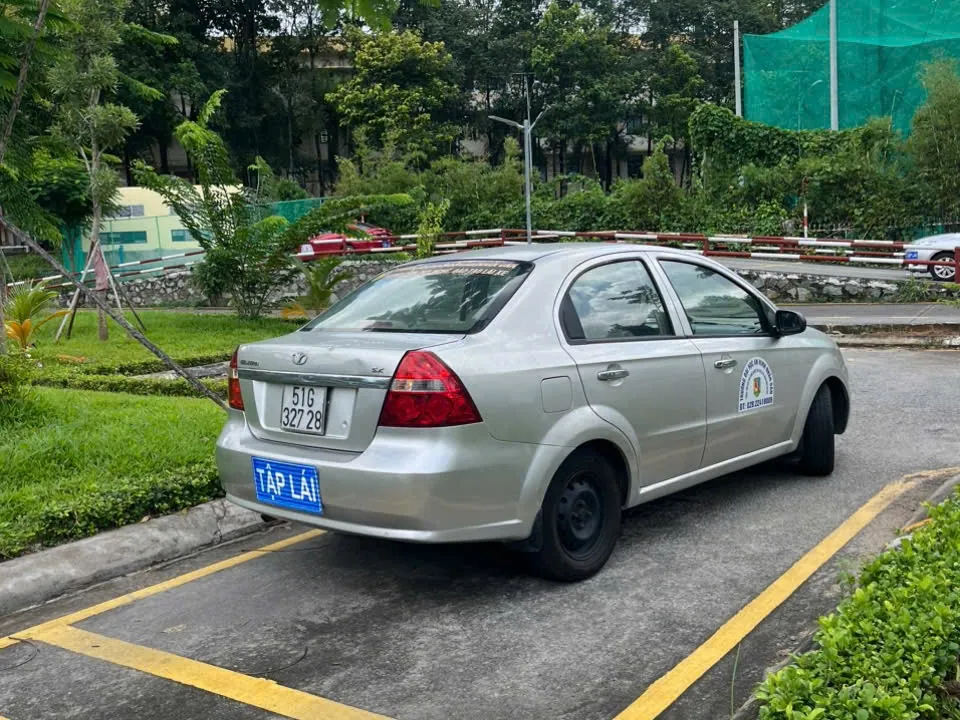 Xe tập lái màu bạc gắn biển TẬP LÁI đỗ trong ô kẻ vạch vàng tại sân tập