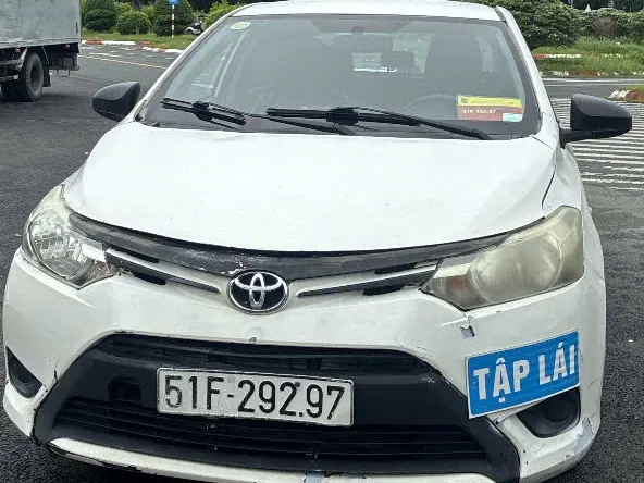 Đầu xe con tập lái màu trắng nhìn chính diện, gắn biển TẬP LÁI màu xanh cạnh biển số