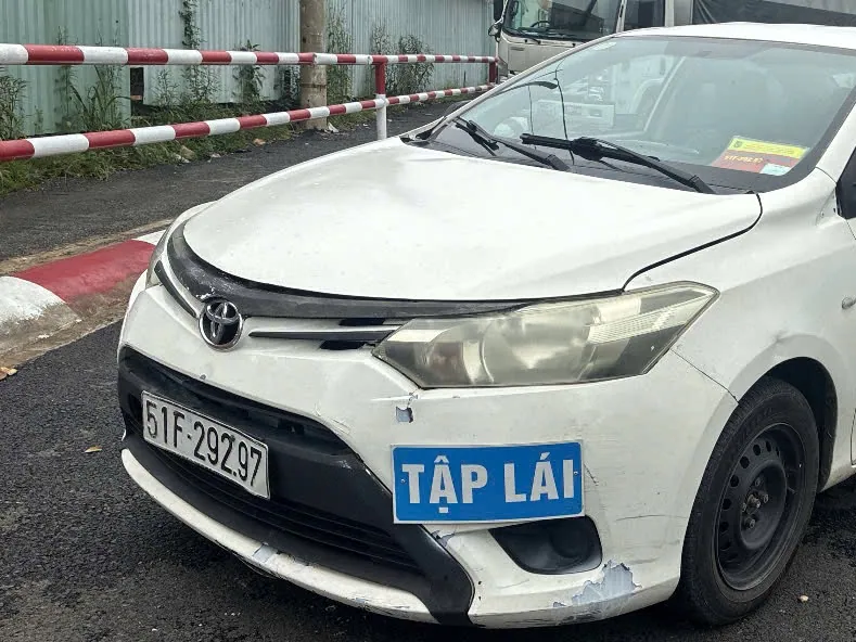 Xe con tập lái màu trắng gắn biển TẬP LÁI đỗ cạnh thanh chắn tại sân trung tâm