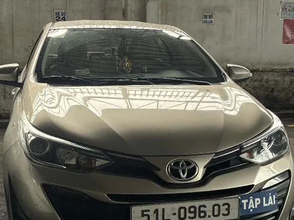 Xe con tập lái màu vàng cát gắn biển TẬP LÁI, đỗ trong nhà xe có bảng đánh số xe