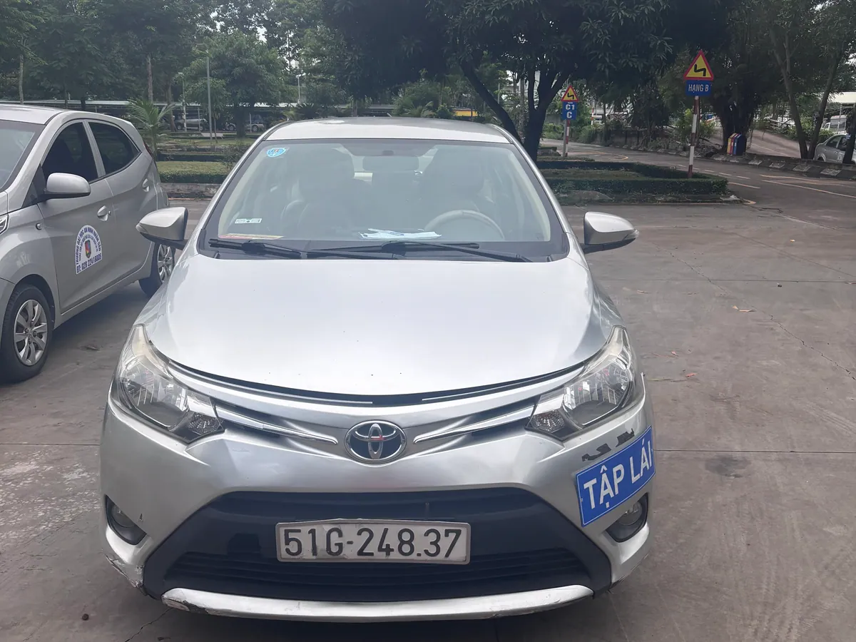 Đầu xe con tập lái Toyota màu bạc nhìn chính diện, biển số 51G-248.37, gắn biển TẬP LÁI màu xanh, đỗ trên sân bê tông của trung tâm
