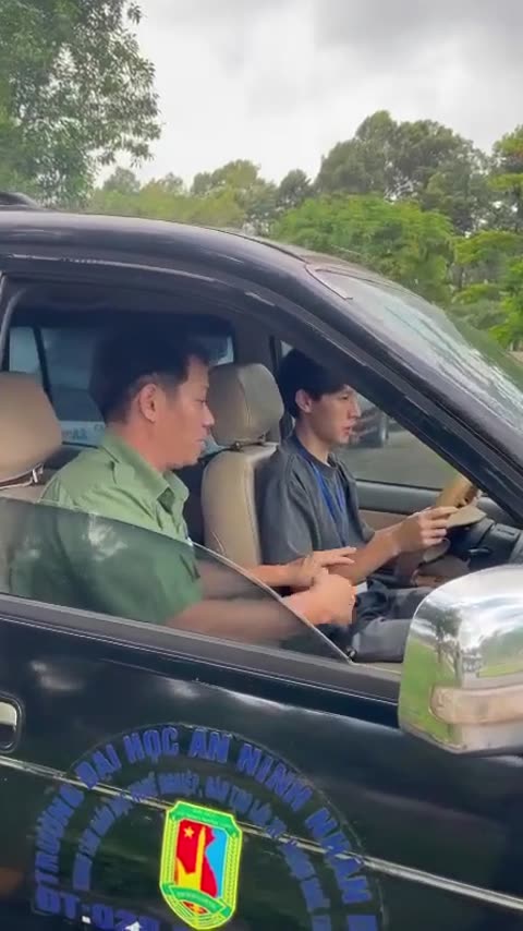 Thầy dạy lái xe ngồi ghế phụ hướng dẫn học viên đang cầm vô lăng trong xe tập lái