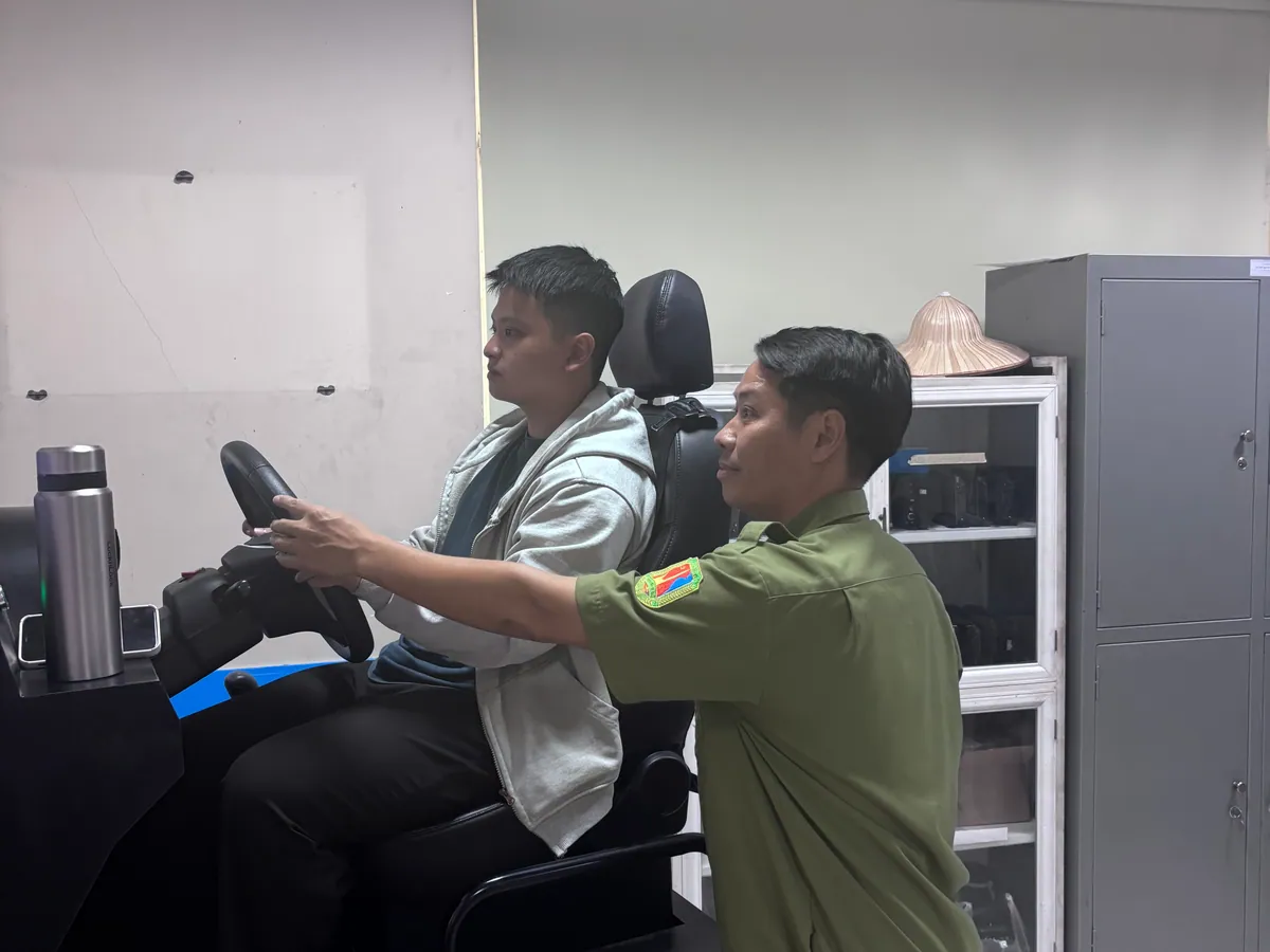 Thầy dạy lái xe cầm vô lăng hướng dẫn thao tác cho học viên ngồi trên cabin học lái